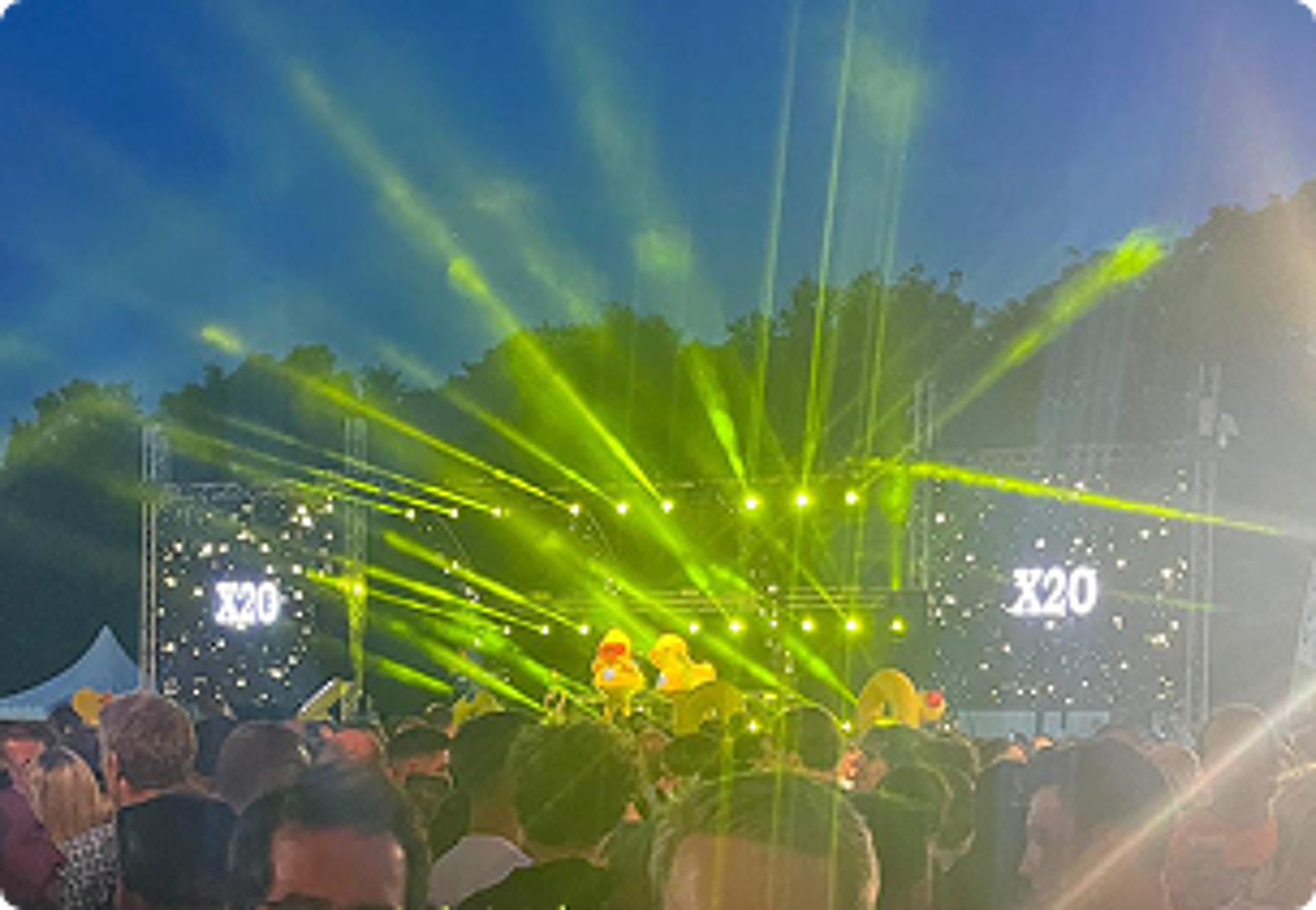 Een avondconcert met felgele lichtstralen en het X²O badkamers-logo prominent zichtbaar op de schermen van het podium.