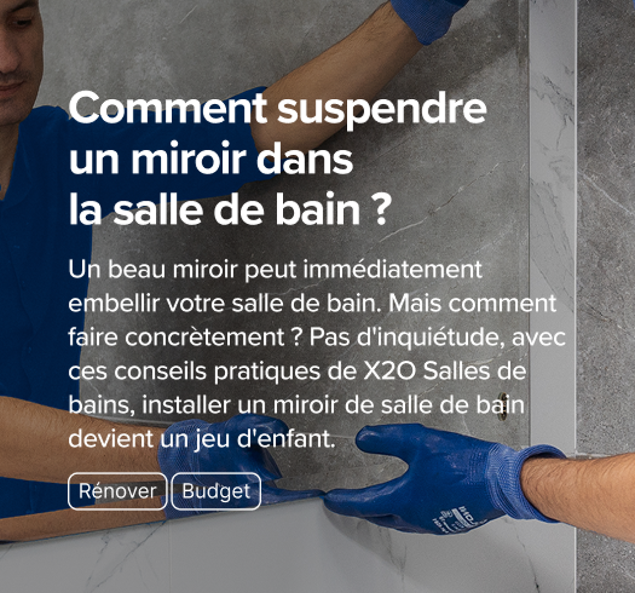 Installateur en tenue bleue fixant un miroir sur un mur de salle de bains effet marbre – un guide pratique de x²o salles de bains.