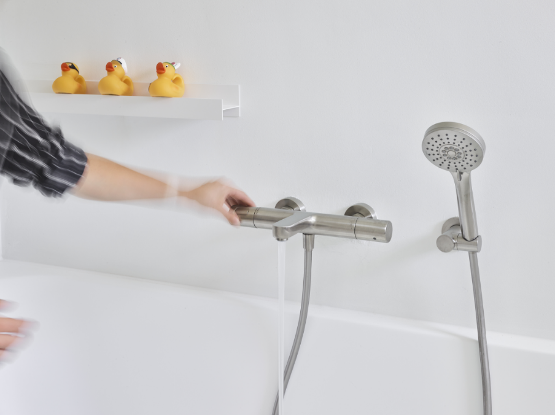 Handbrause mit Wasserstrahl an einem weißen Badewannenrand.