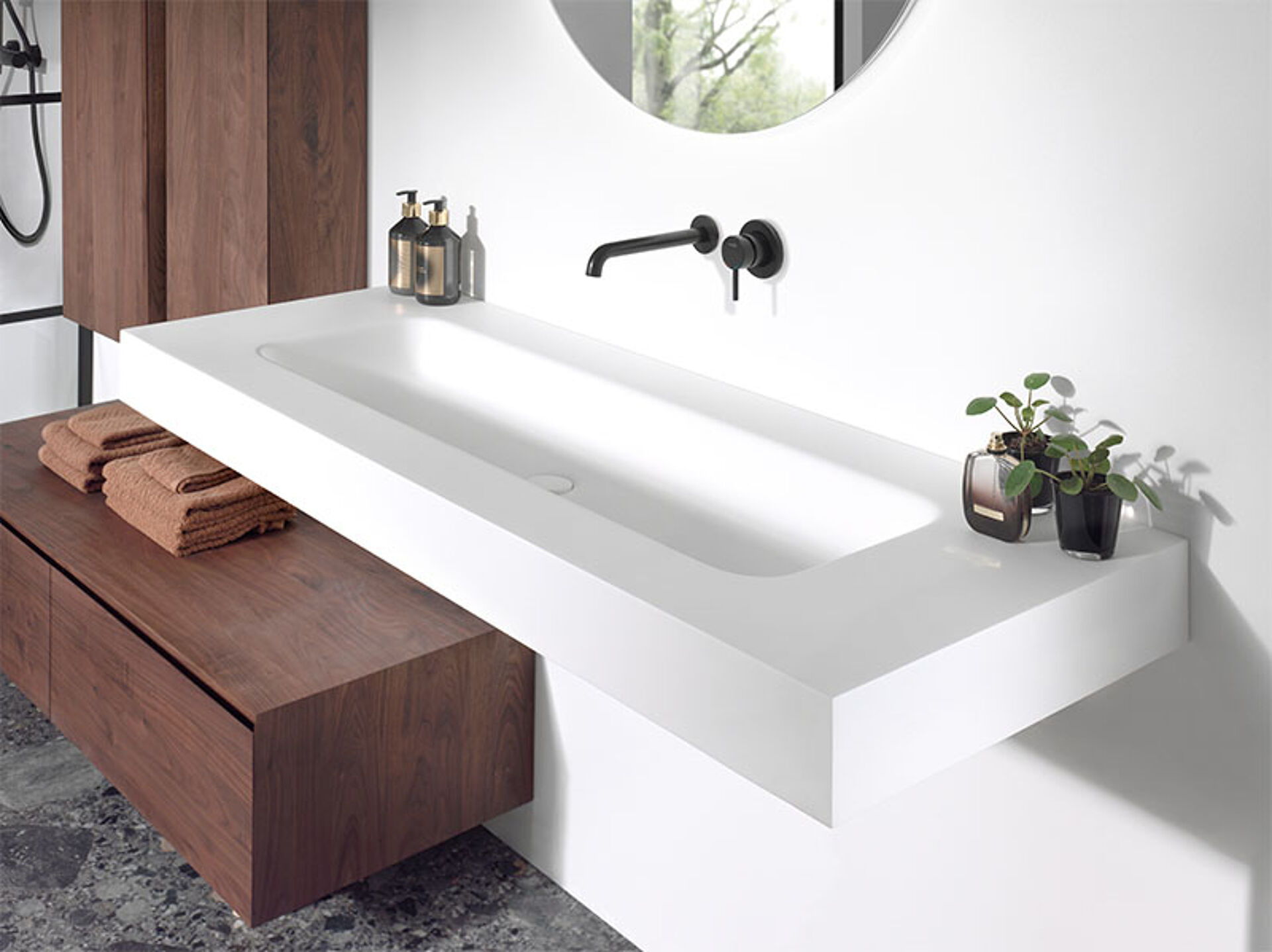 Moderne witte wastafel met geïntegreerde spoelbak en zwarte wandkraan, gecombineerd met houten meubel.