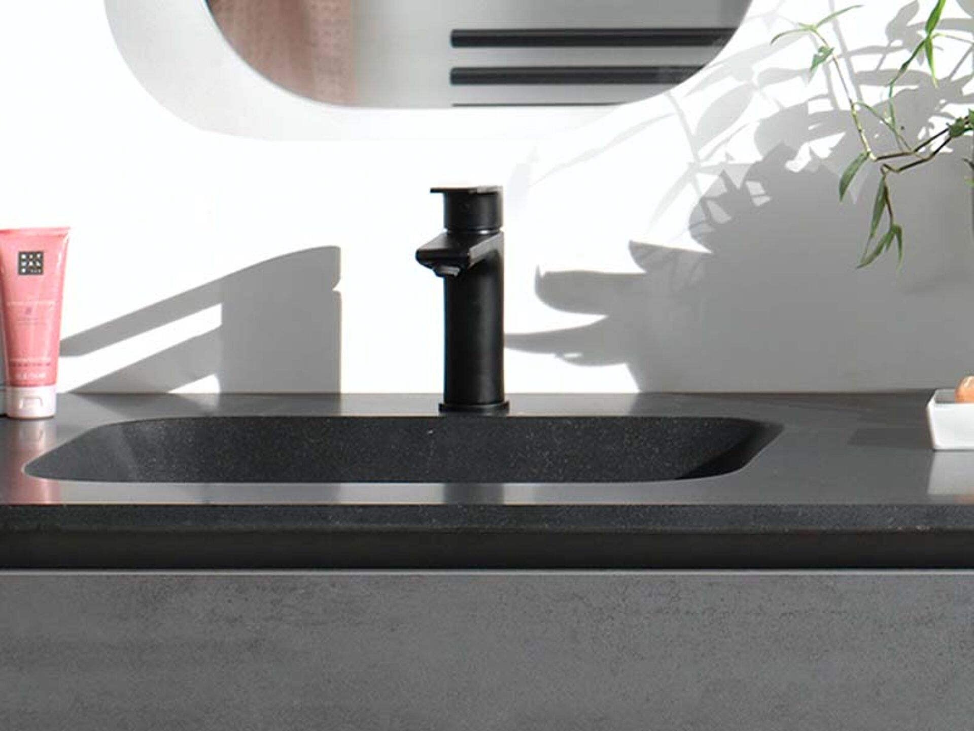 Schwarzes Einbauwaschbecken mit mattschwarzer Armatur auf dunkler Platte, modernes und stilvolles Design.
