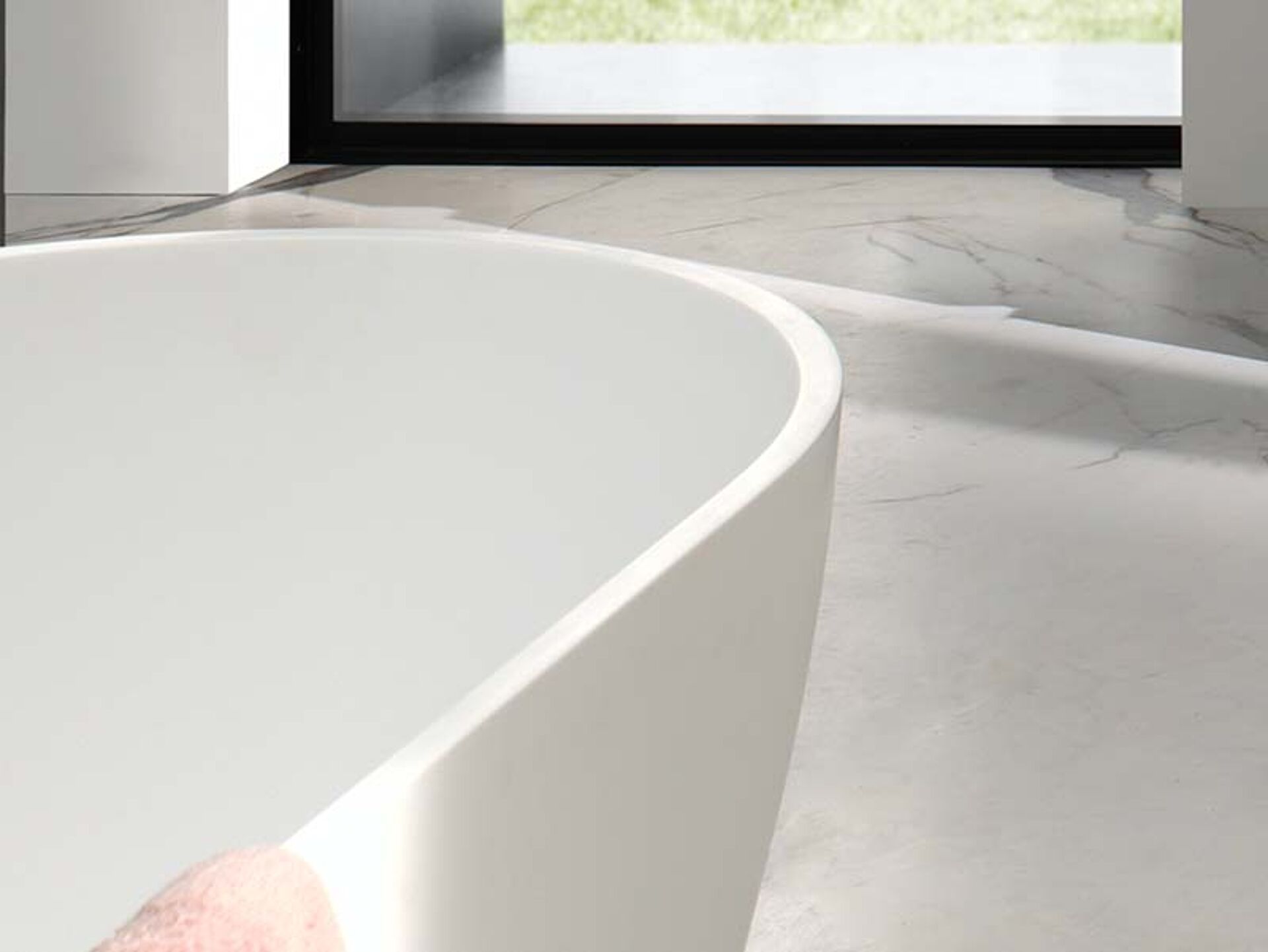 Freistehende weiße Badewanne mit runden Formen, platziert auf Marmorboden mit natürlichem Licht.
