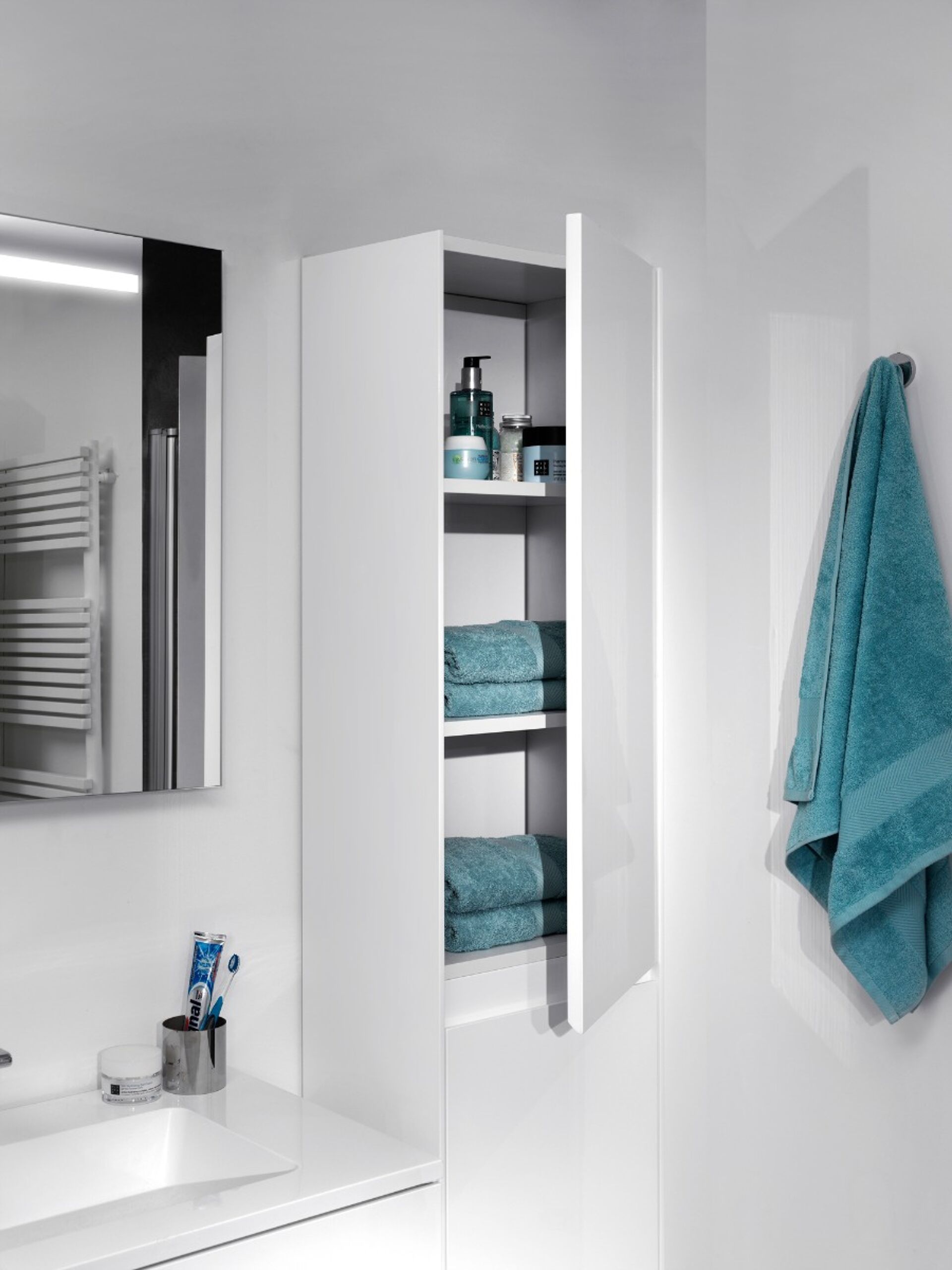 Weißer Badezimmerschrank mit geöffneter Tür, gefüllt mit Handtüchern und Pflegeprodukten.