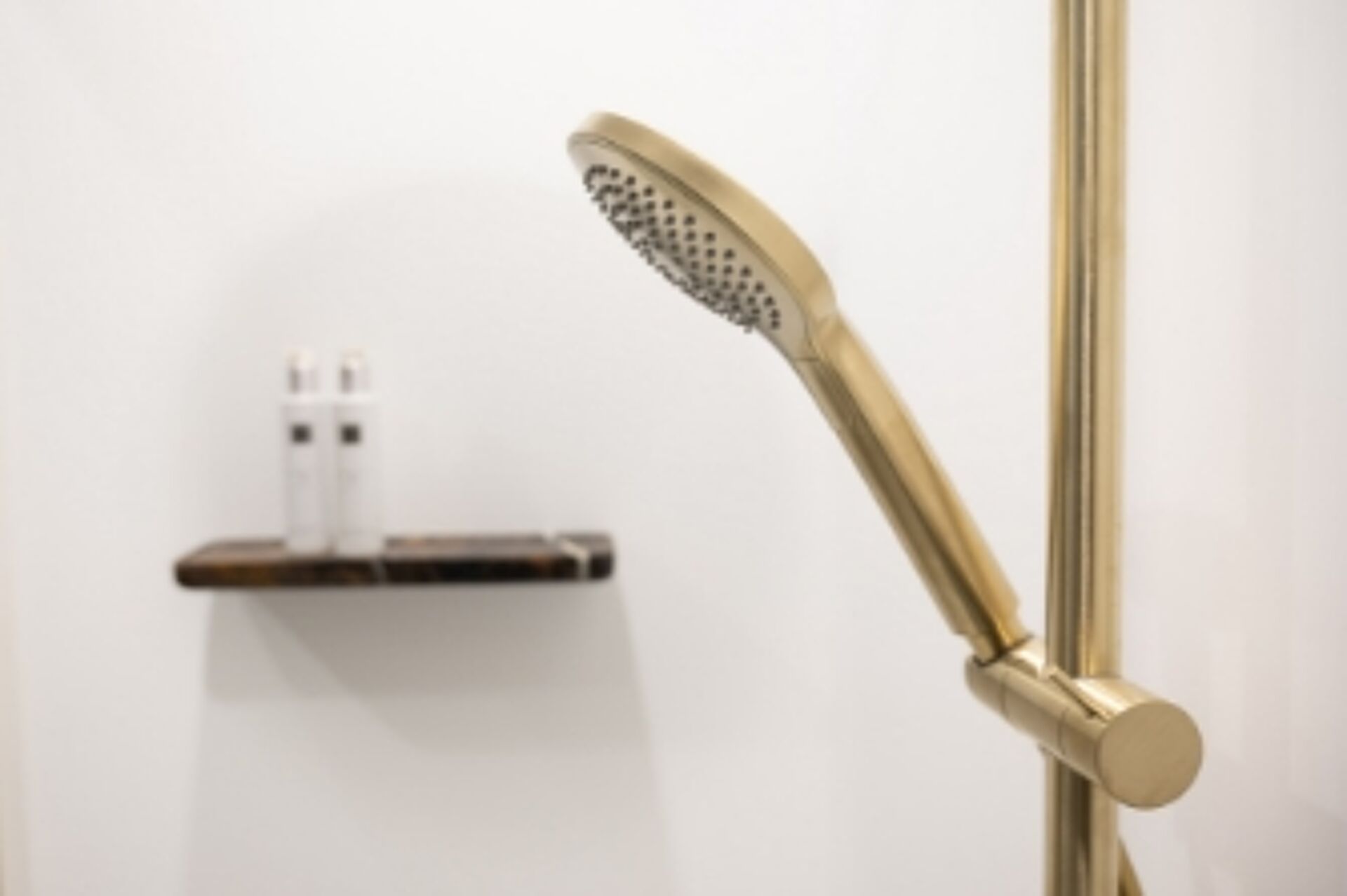 Luxuriöse Dusche mit goldener Handbrause und Marmorablage vor einer weißen Wand für eine elegante Optik.