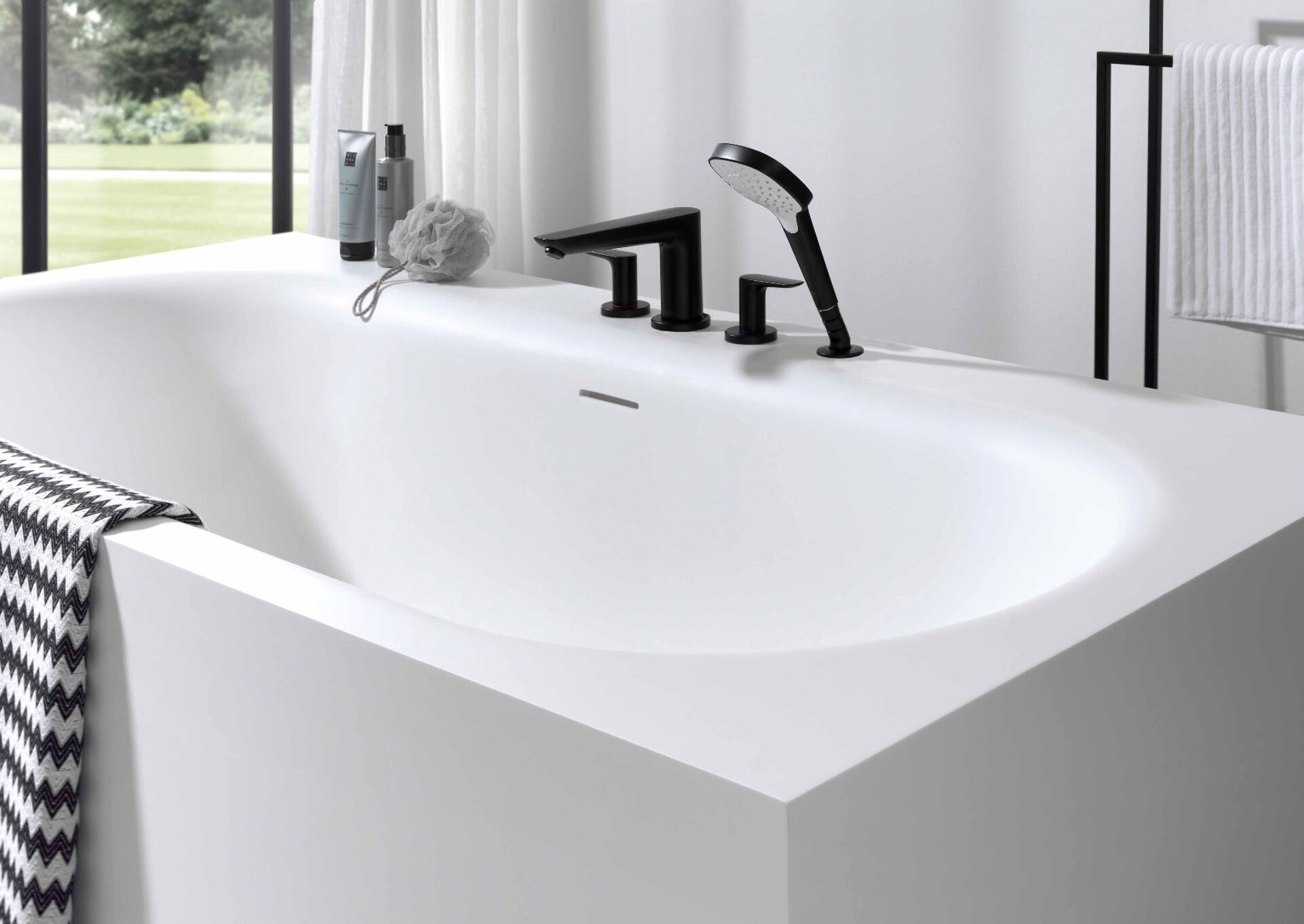  Moderne weiße Badewanne mit mattschwarzen Armaturen und Handbrause in einem minimalistischen Badezimmer.