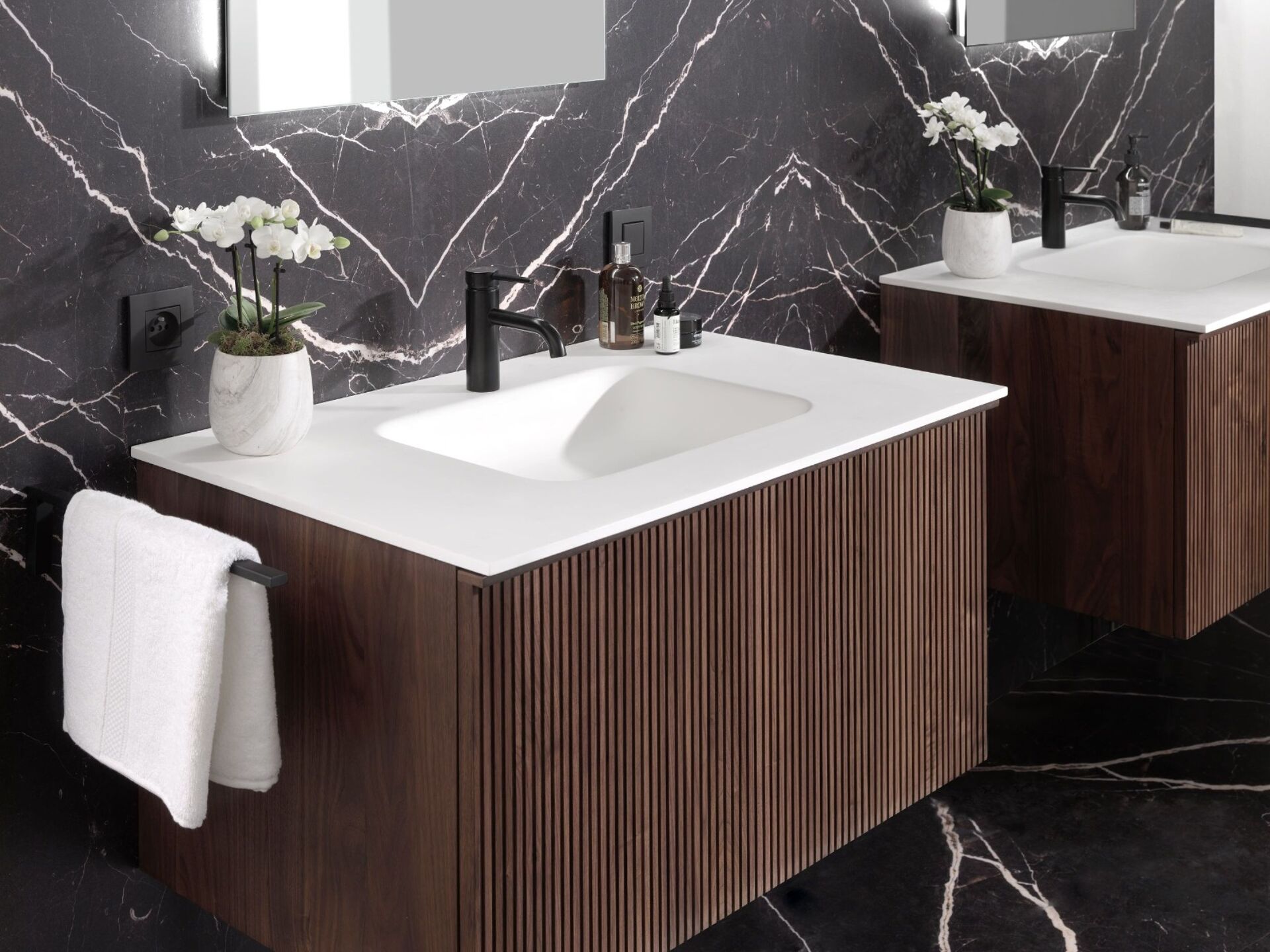 Luxe badkamer met houten wastafelmeubels, zwarte marmeren muren en moderne zwarte kranen.