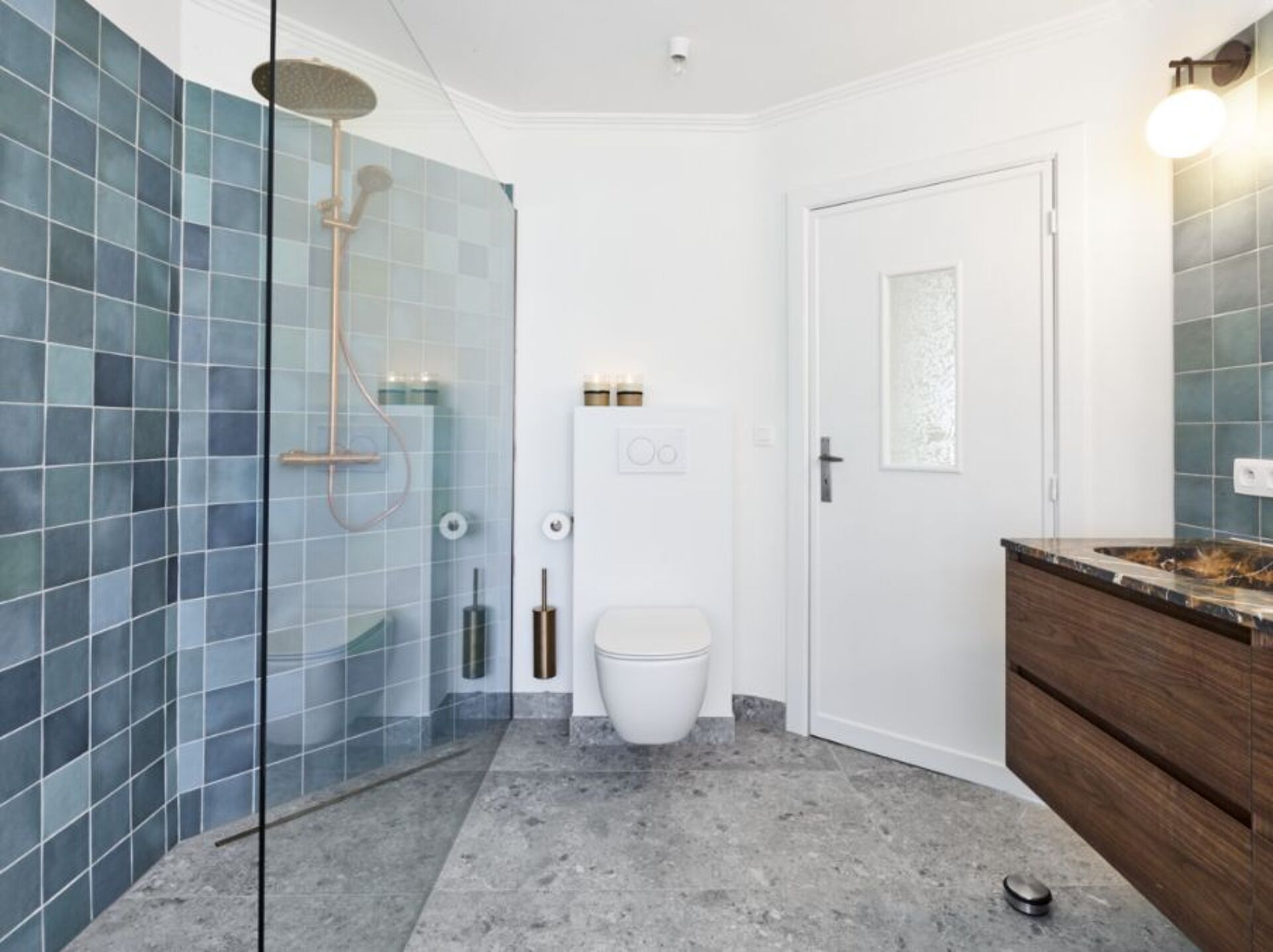 Badezimmer mit Glasdusche, Toilette, grauem Marmorboden, blauen Fliesen und Holzwaschbecken.