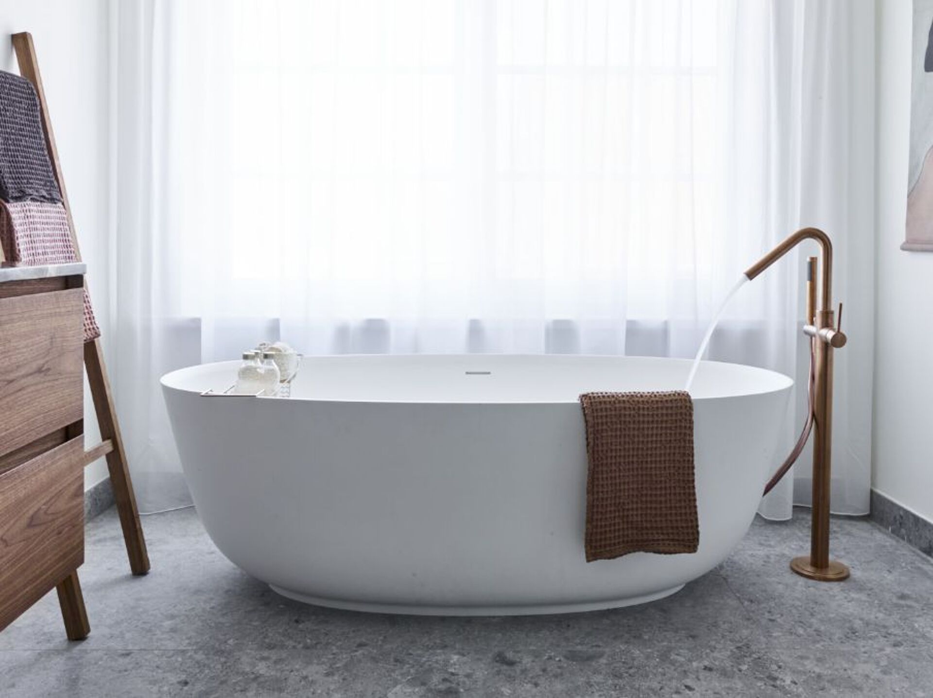 Badezimmer mit freistehender Badewanne, goldenem Wasserhahn und grauem Marmorboden.