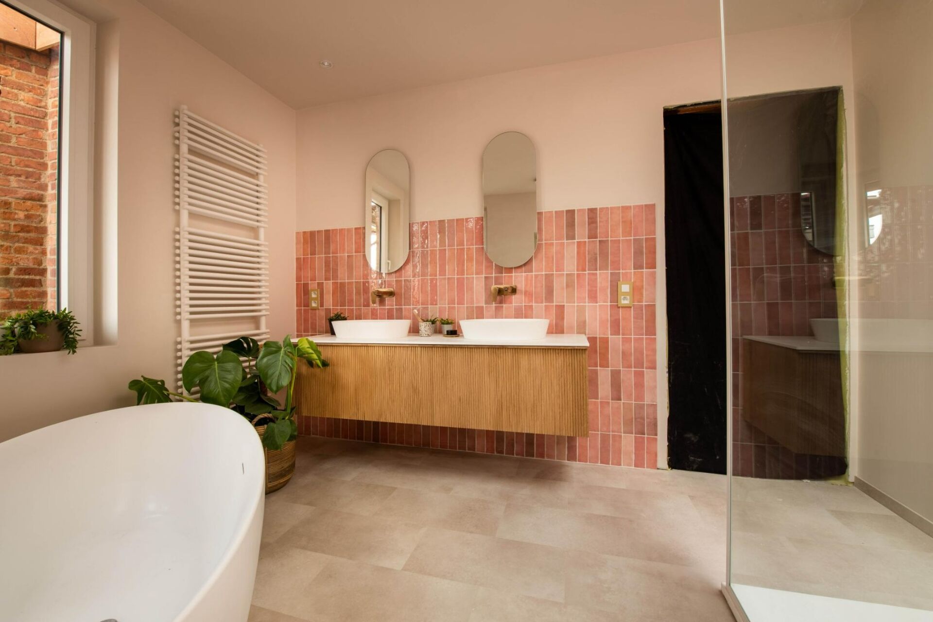 Moderne badkamer met houten wastafelmeubel, dubbele wastafels, tegelwand en glazen douchewand.