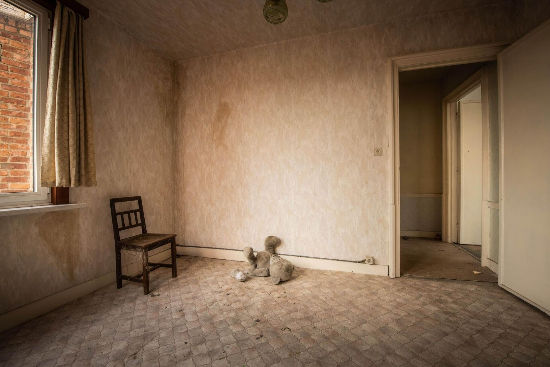 Verwaarloosde kamer met een houten stoel, teddybeer op de vloer en vervaagde muren