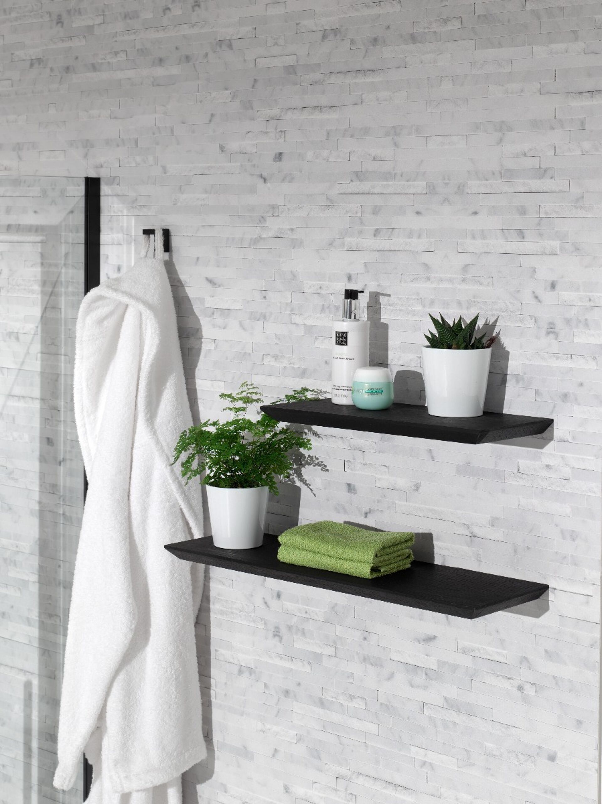 Ein modernes Badezimmer mit einer weißen gefliesten Wand, einem weißen Bademantel und zwei Regalen mit Handtüchern und Pflanzen