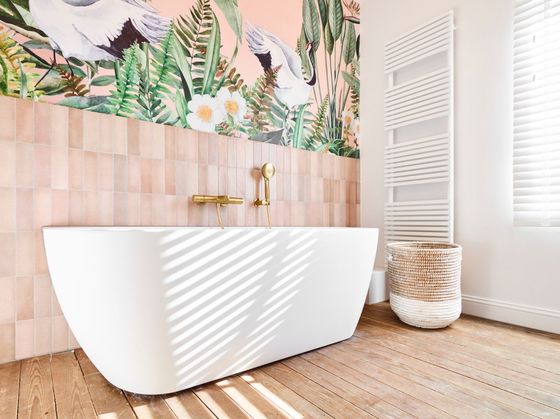 Moderne Badezimmer mit einer weißen Badewanne, goldenen Wasserhähnen und einer tropischen Wandgestaltung in Rosatönen mit Blumen und Vögeln