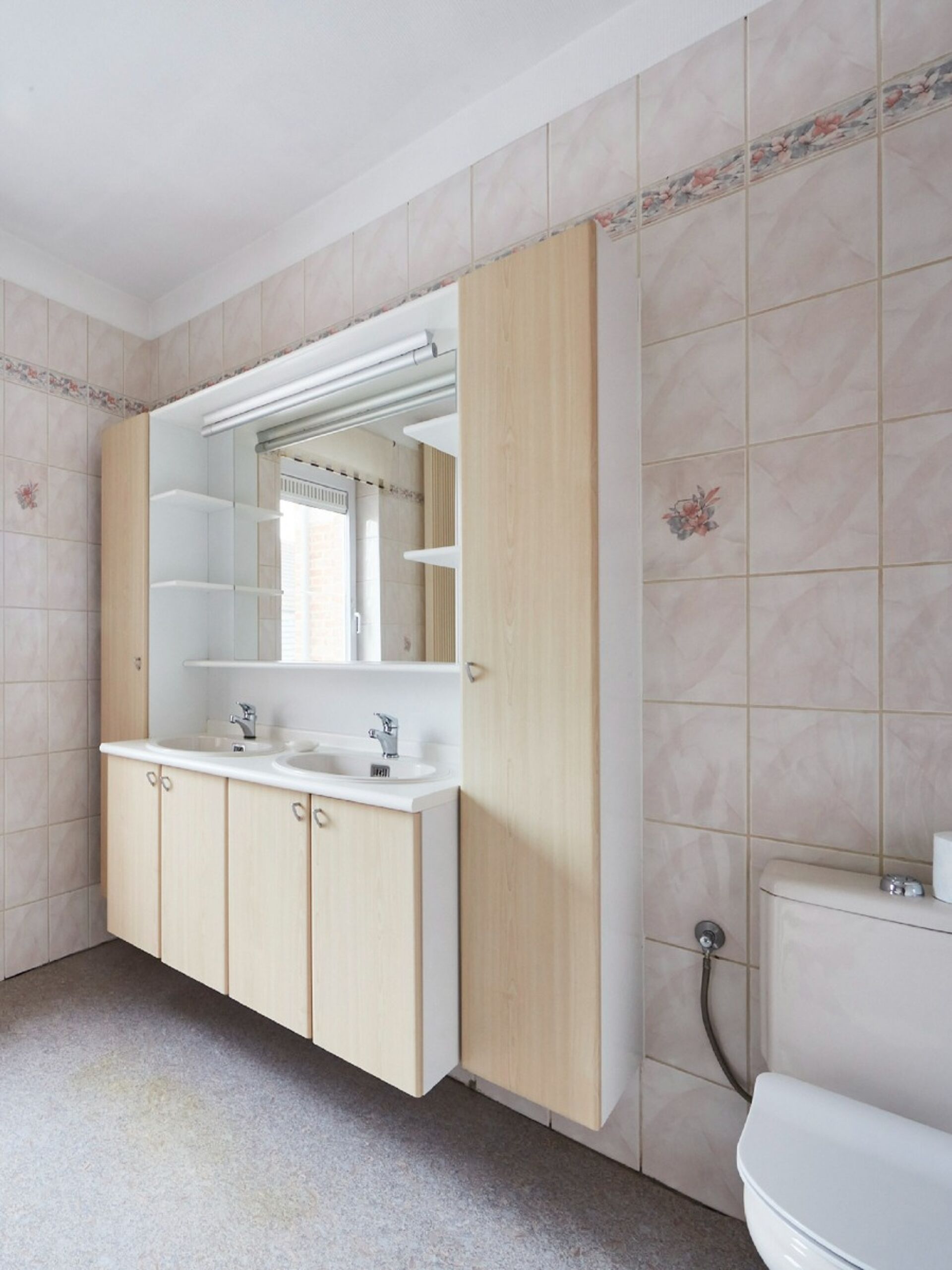 Badezimmer mit Doppelwaschbecken, Toilette und Aufbewahrungsmöbel mit beigen Fliesen und neutralem Bodenbelag