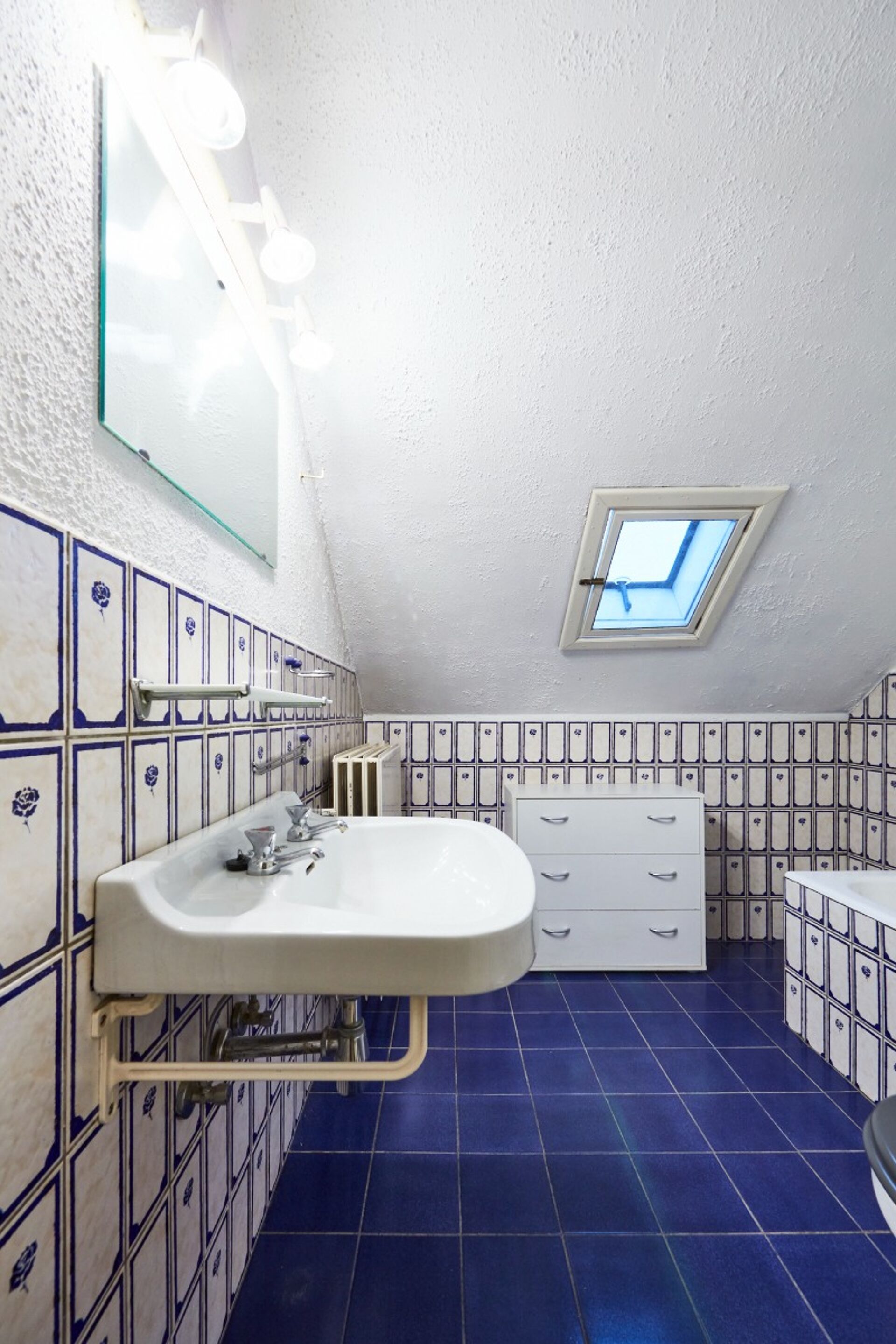 Badezimmer mit weißem Waschbecken, blauen Fliesen und Dachfenster