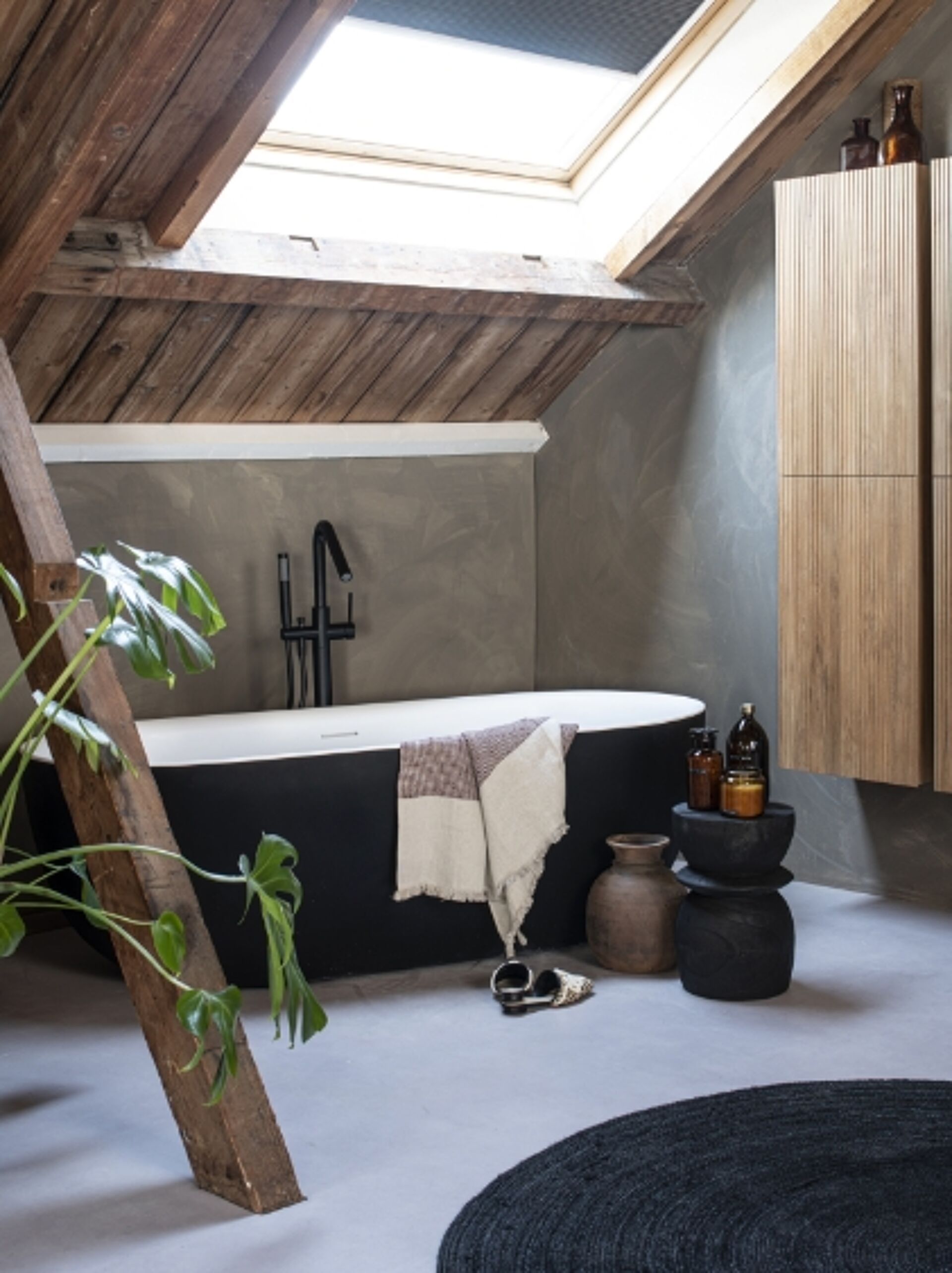 Baignoire noire autoportante avec robinet noir moderne, meuble en bois et plantes dans une salle de bain rustique.