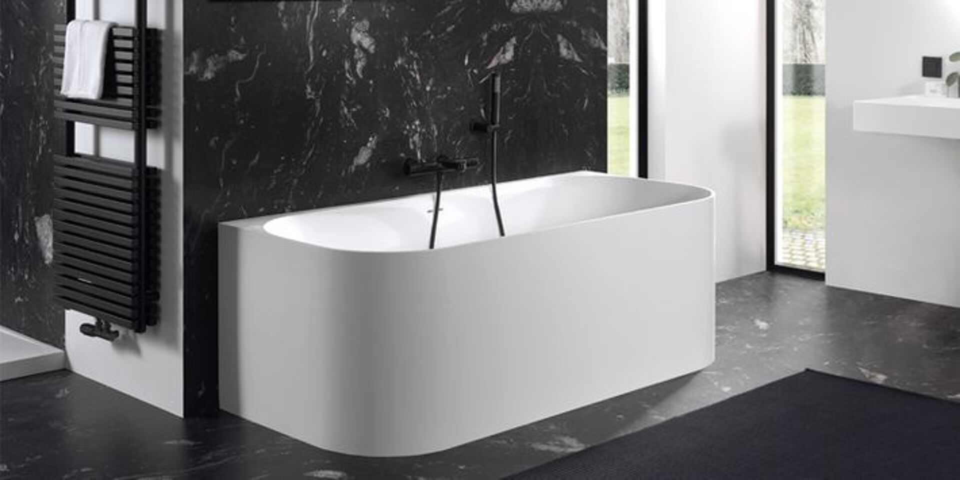 Freistehende Badewanne mit schwarzer Marmorwand und schwarzem Wasserhahn im modernen Badezimmer.