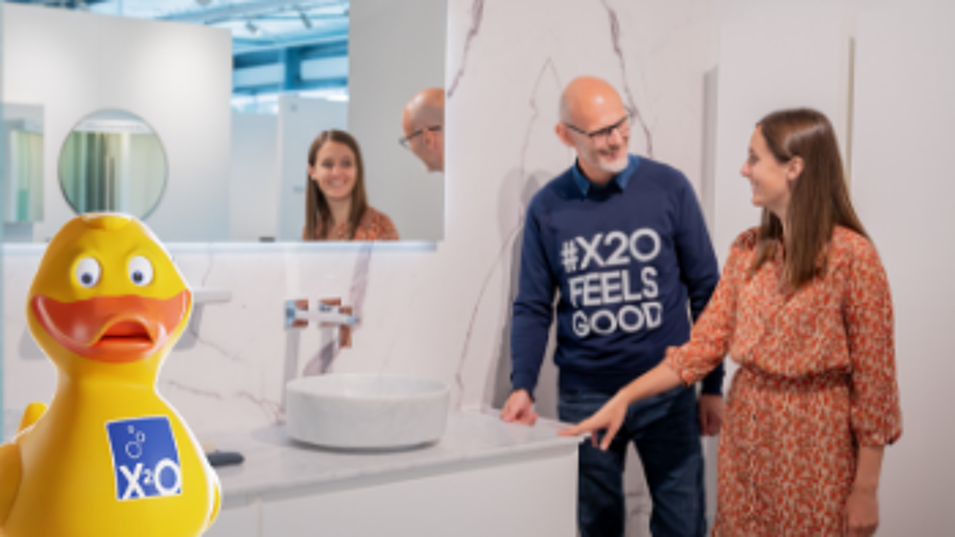 Vasque blanche sur plan en marbre dans showroom avec clients souriants et canard X2O
