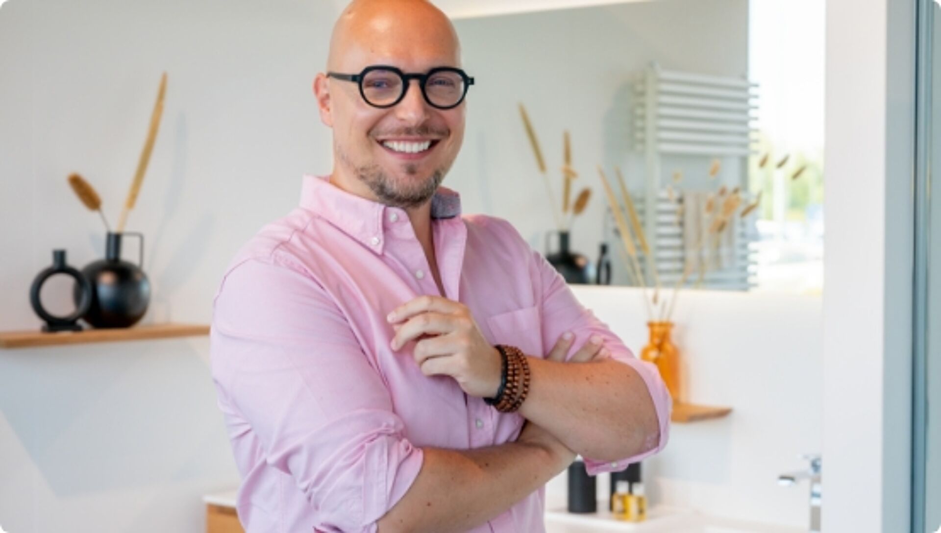 Glimlachende man met bril in moderne badkamer met warme decoratie en natuurlijke accenten